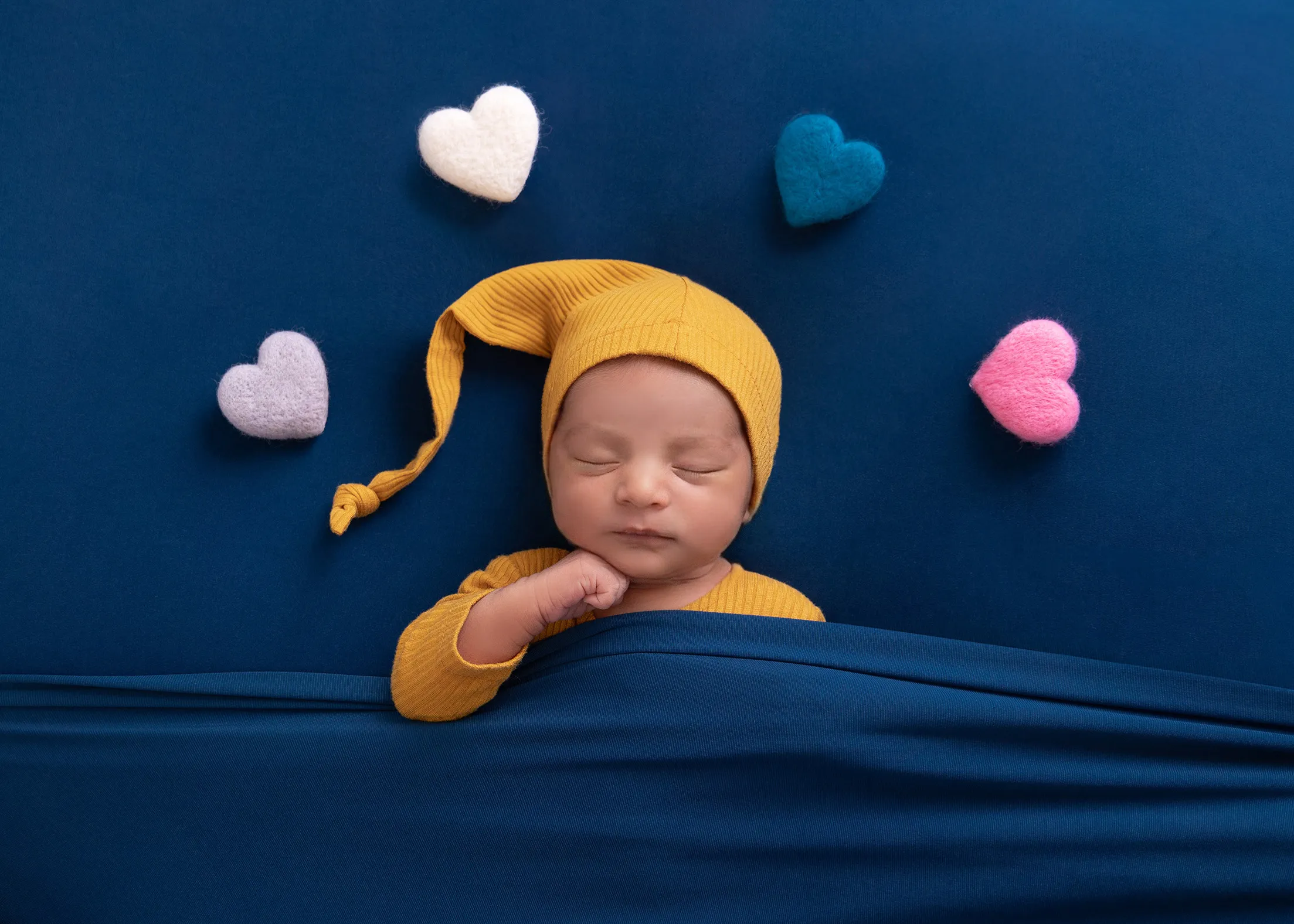 Newborn in a yellow cap sleeping among soft felt hearts
