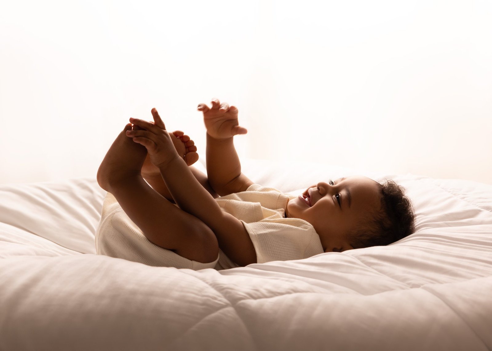 A laughing baby in soft morning light, holding her feet