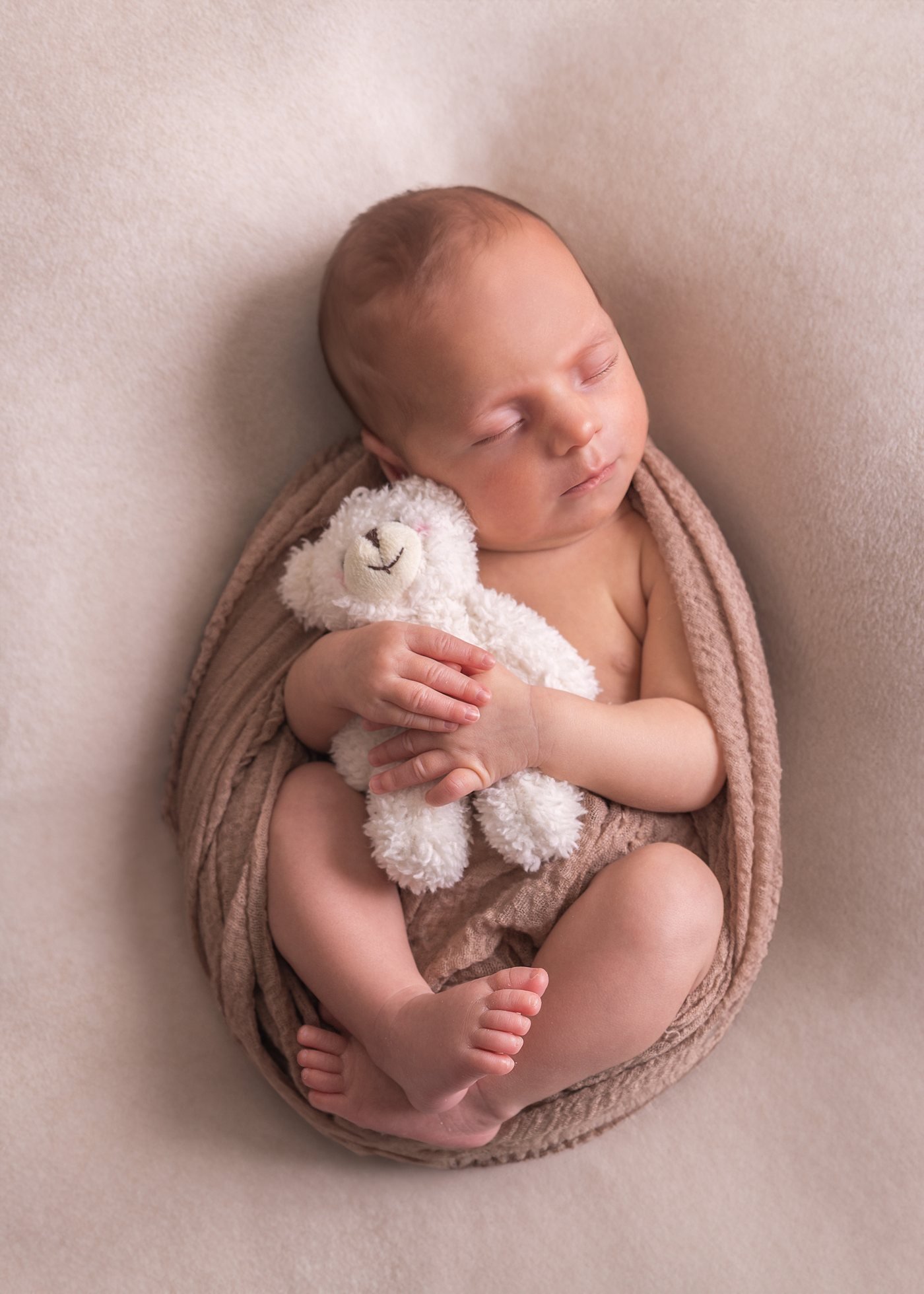 Sleeping newborn hugging a small teddy bear